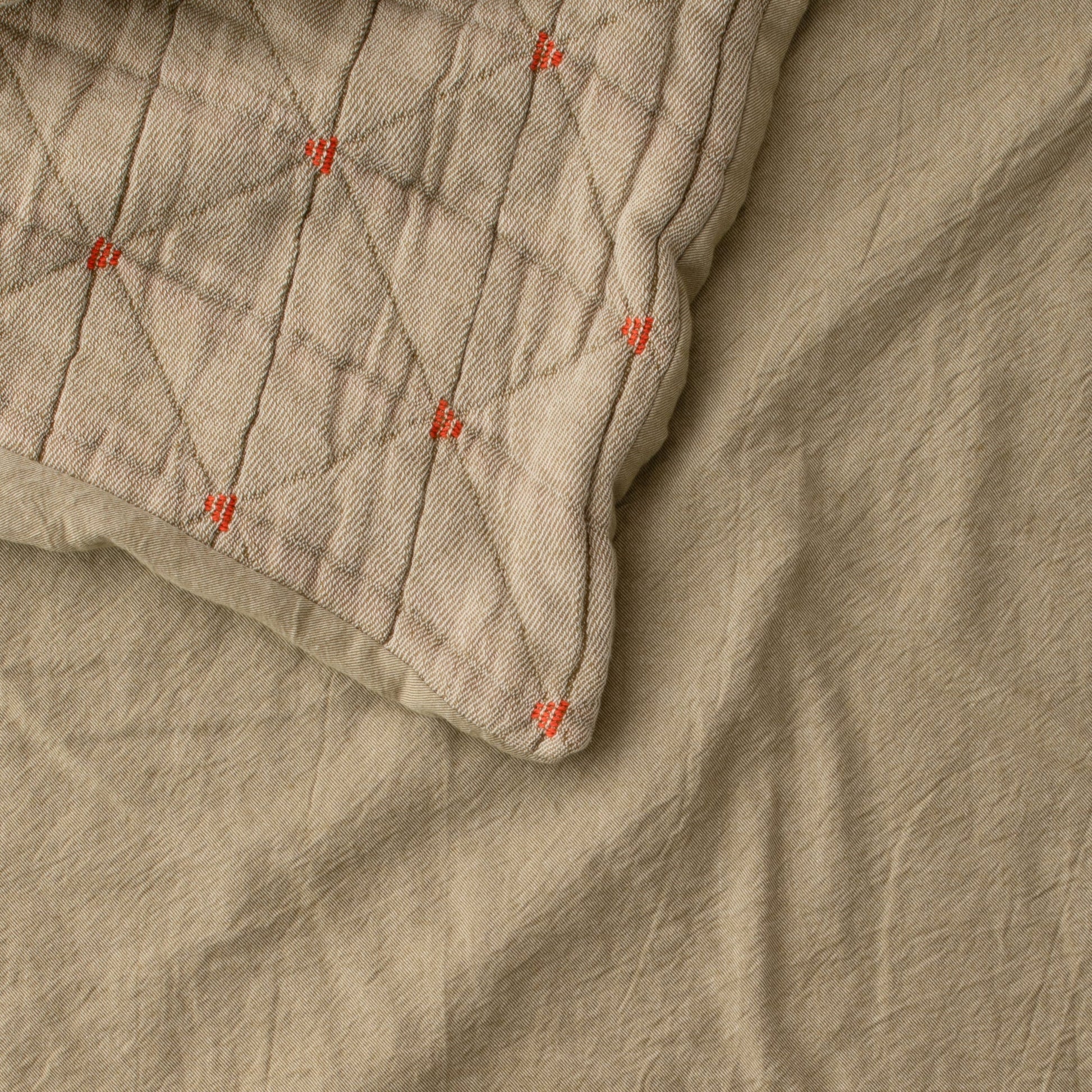 Close-up of Peak Stitch Duvet showing triangular matelasse quilting and red yarn-tie stitches on beige cotton twill