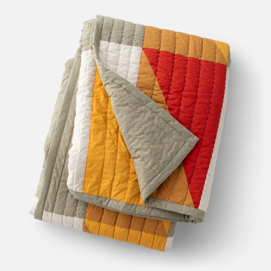 Overhead view of folded Modern Rooftops quilt showing red, mustard, gray and white geometric blocks and vertical quilting