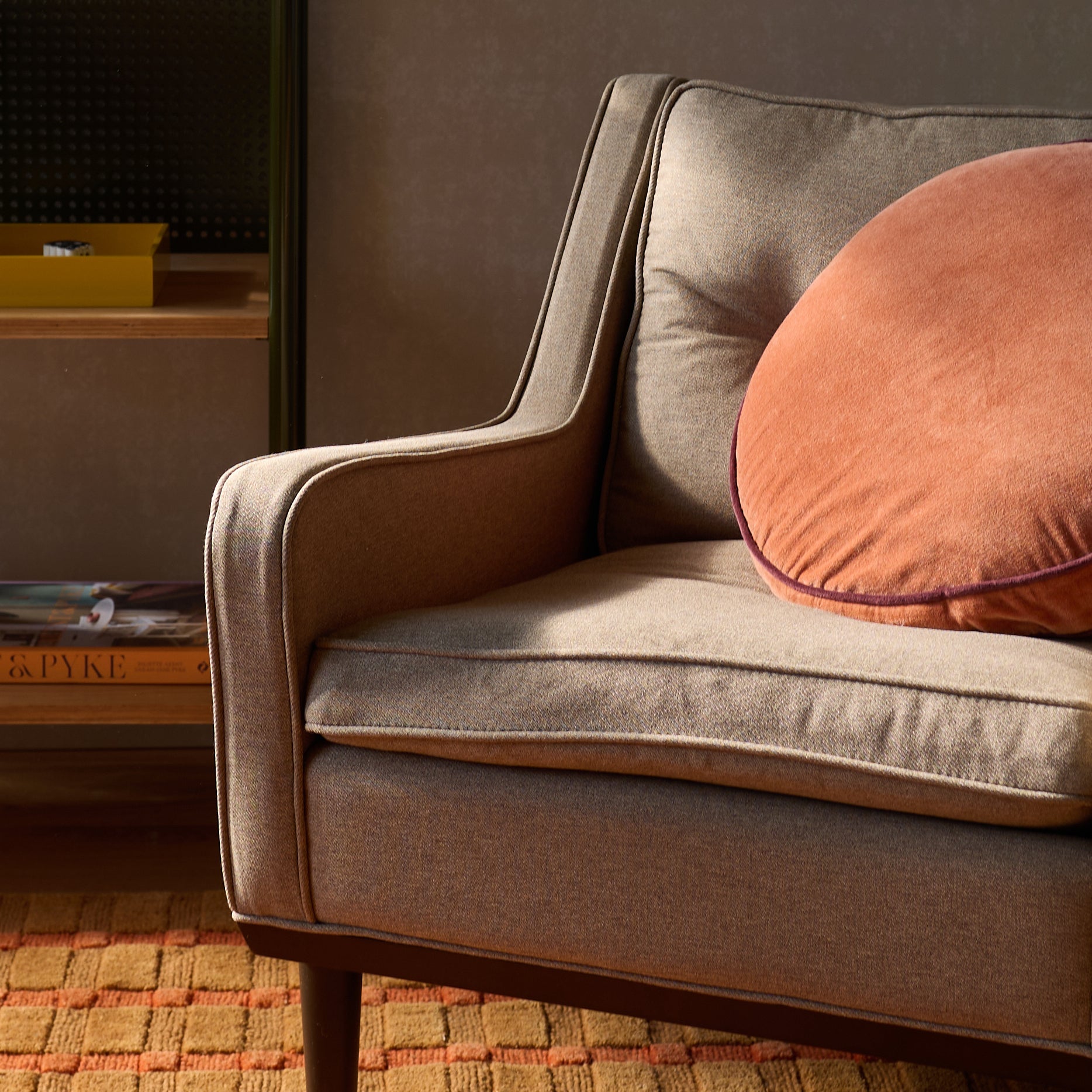 Three-quarter view of Velvet Piped Pillow in raisin velvet with contrast piping on a gray upholstered chair